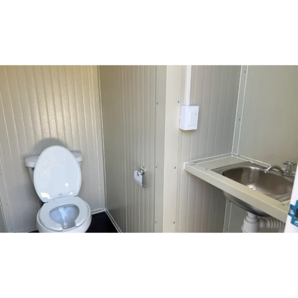 Interior de remolque sanitario 12x7 pies con inodoro, lavabo de acero inoxidable y paredes metálicas beige, diseñado por Soluciones Móviles.