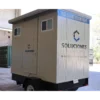 Remolque sanitario móvil de 12x7 pies color beige y gris con logotipo de Soluciones Móviles, diseñado para venta o renta, ubicado en un almacén industrial.